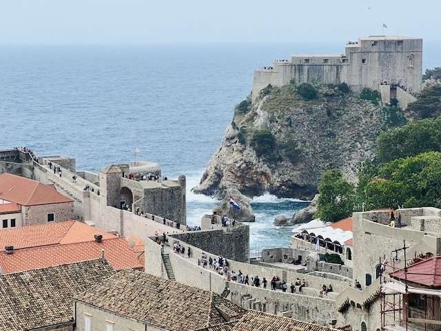 Many visitors walking along the wall surrounding Dubrovnik overlooking the fort on the opposite hill